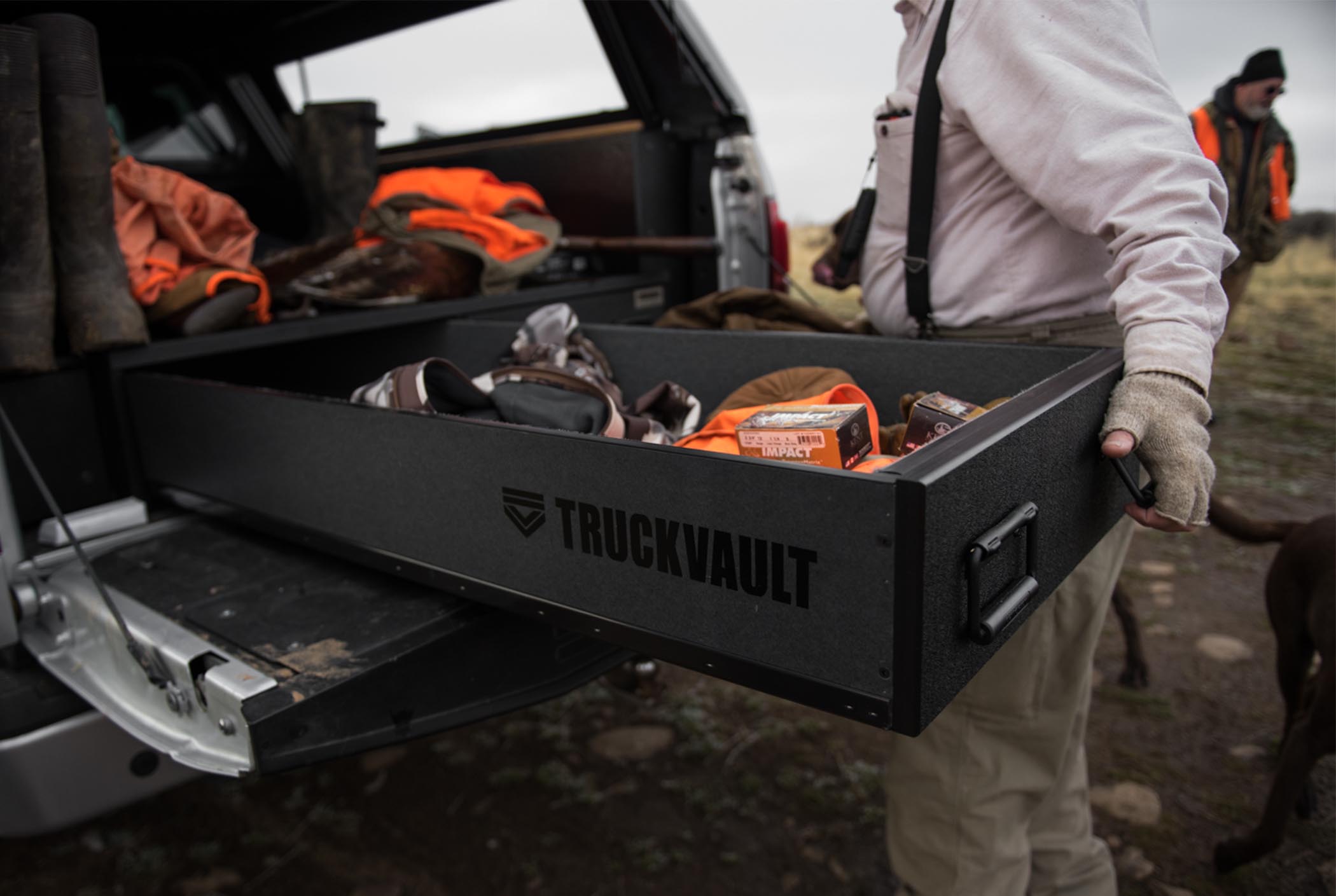 A man opening a covered bed TruckVault system that is securing upland bird hunting equipment.