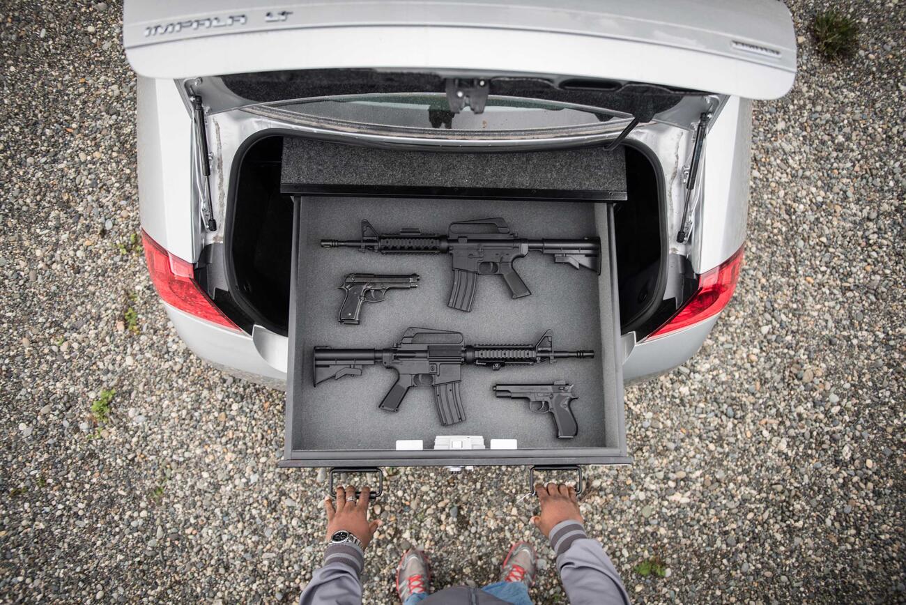 A silver Chevy Impala with a person pulling out a TruckVault drawer with guns.