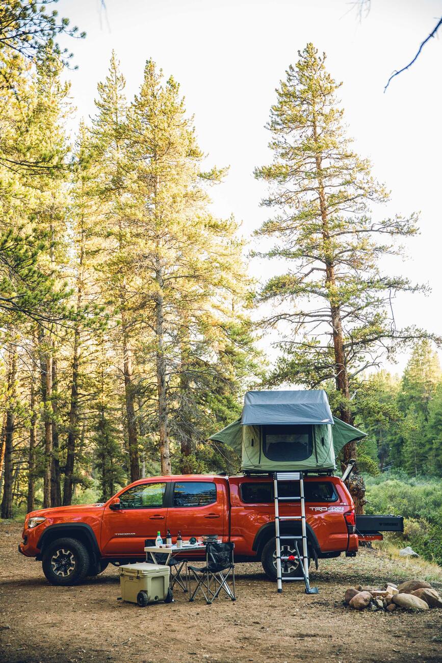 A green tent on top of a red Toyota Tacoma. There is an open TruckVault in the bed of the bed.