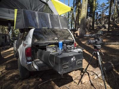 A white Toyota Tundra parked in the woods with a TruckVault filled with camera equipment.