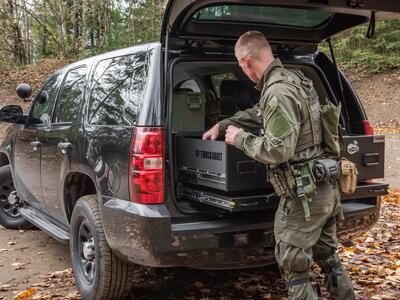 A man wearing tactical clothing grabbing equipment out of a TruckVault inside of a black Chevy Tahoe.