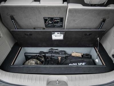 An open Kia Sedona FloorVault filled with a gun and other police gear.