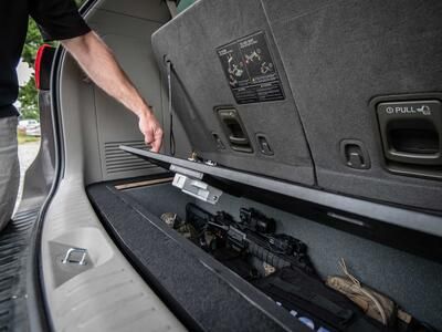 A man opening a Kia Sedona FloorVault filled with a gun and other police gear.