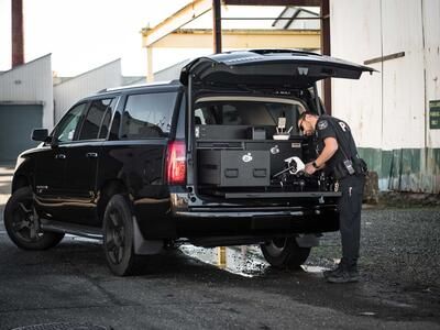 A police officer working on his drone on a pull-out table attached to his black Chevy Suburban.