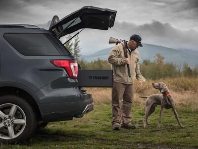 Hunter with gun and dog standing next to SUV with open hatch and TruckVault secure storage drawer extended