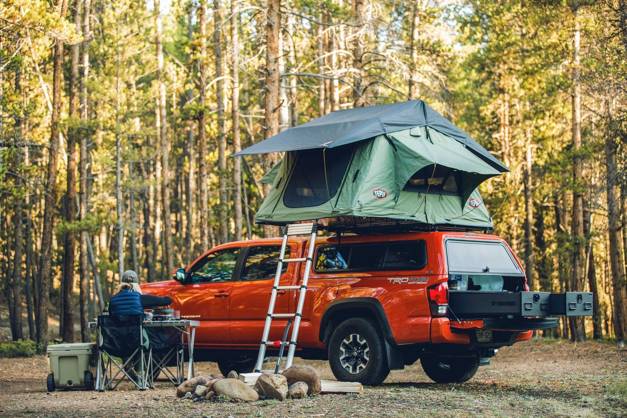 A green tent on top of a red truck. There is an open TruckVault in the back of the truck.