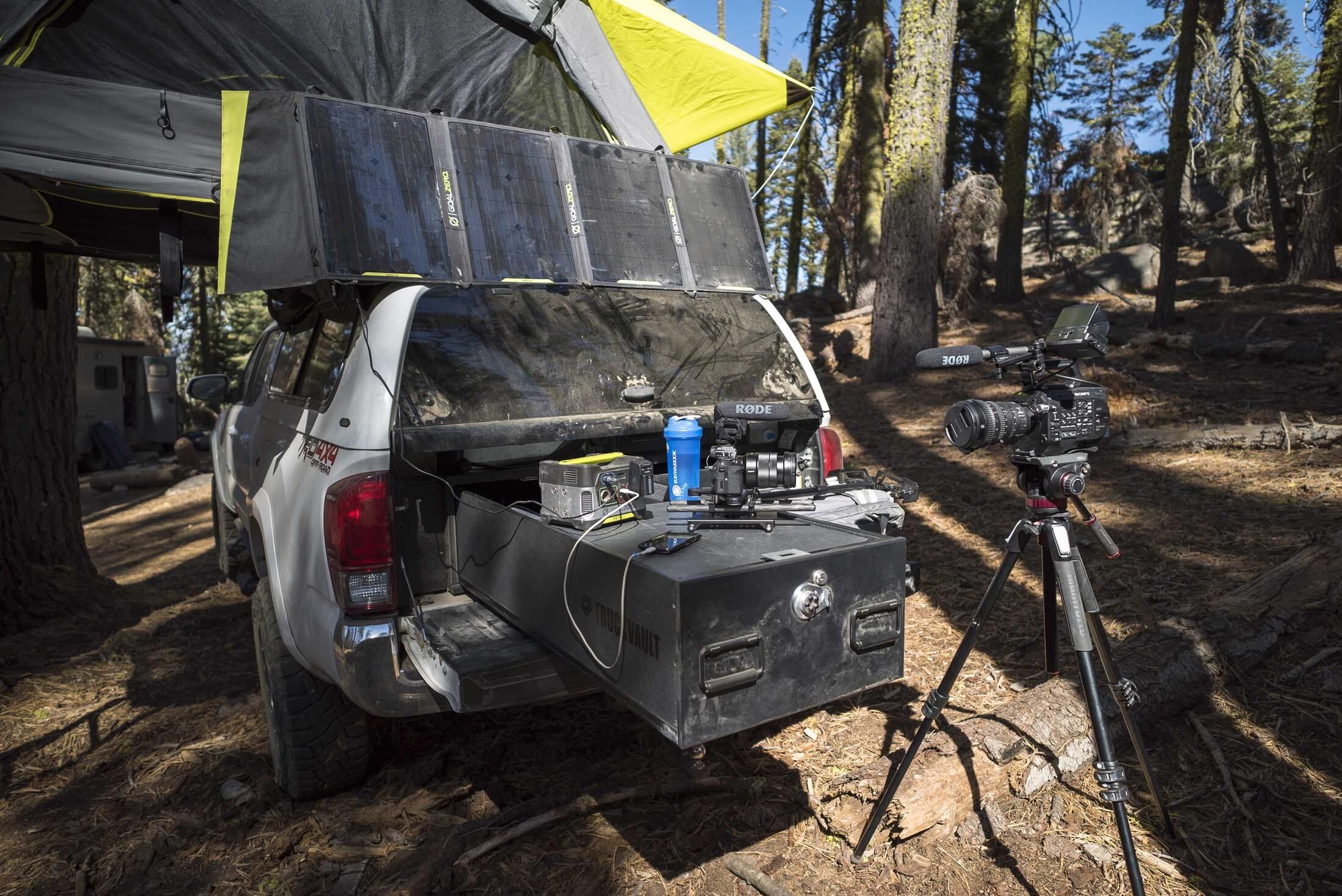 A white Toyota Tundra parked in the woods with a TruckVault filled with camera equipment.
