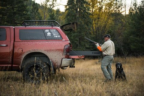 A hunter pulls his shot gun from TruckVault secure truckbed storage solution drawer installed in a Dodge Ram while his hunting bird dog sits by his feet 