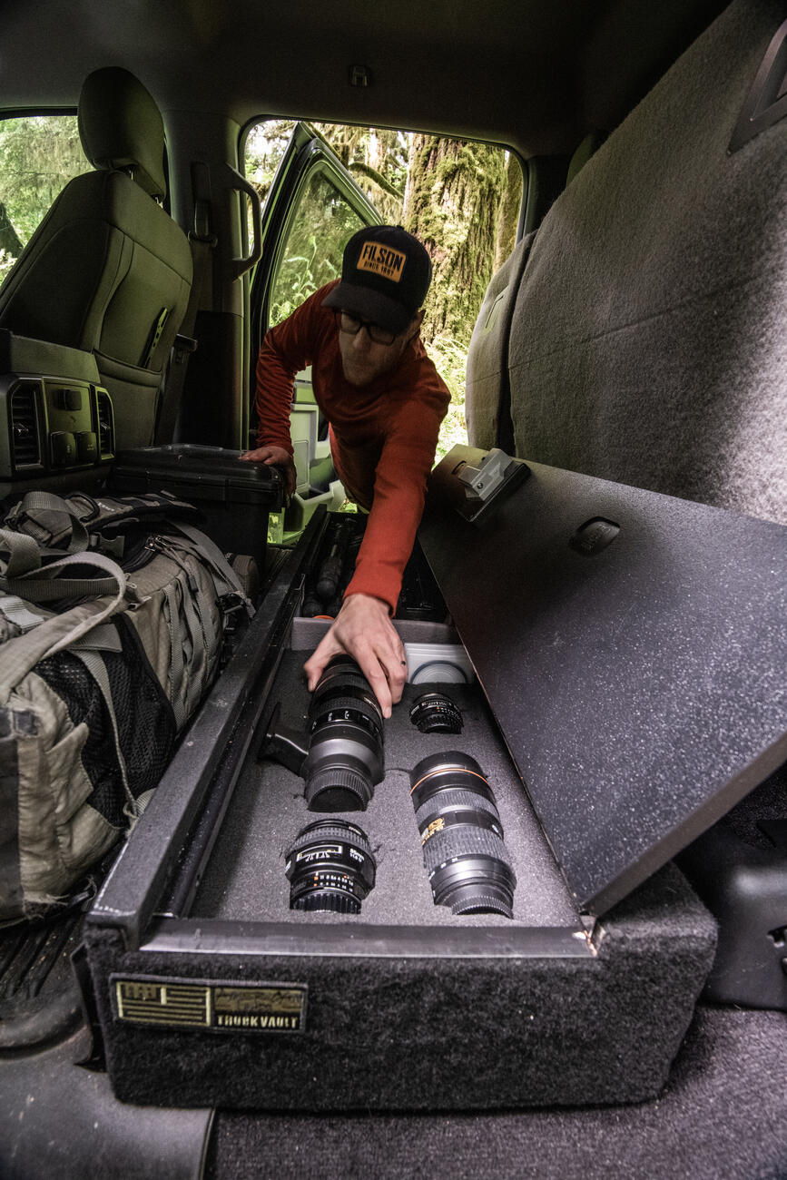 photographer reaches into SeatVault to remove one of many camera lenses from SeatVault storage system under seat in pickup truck