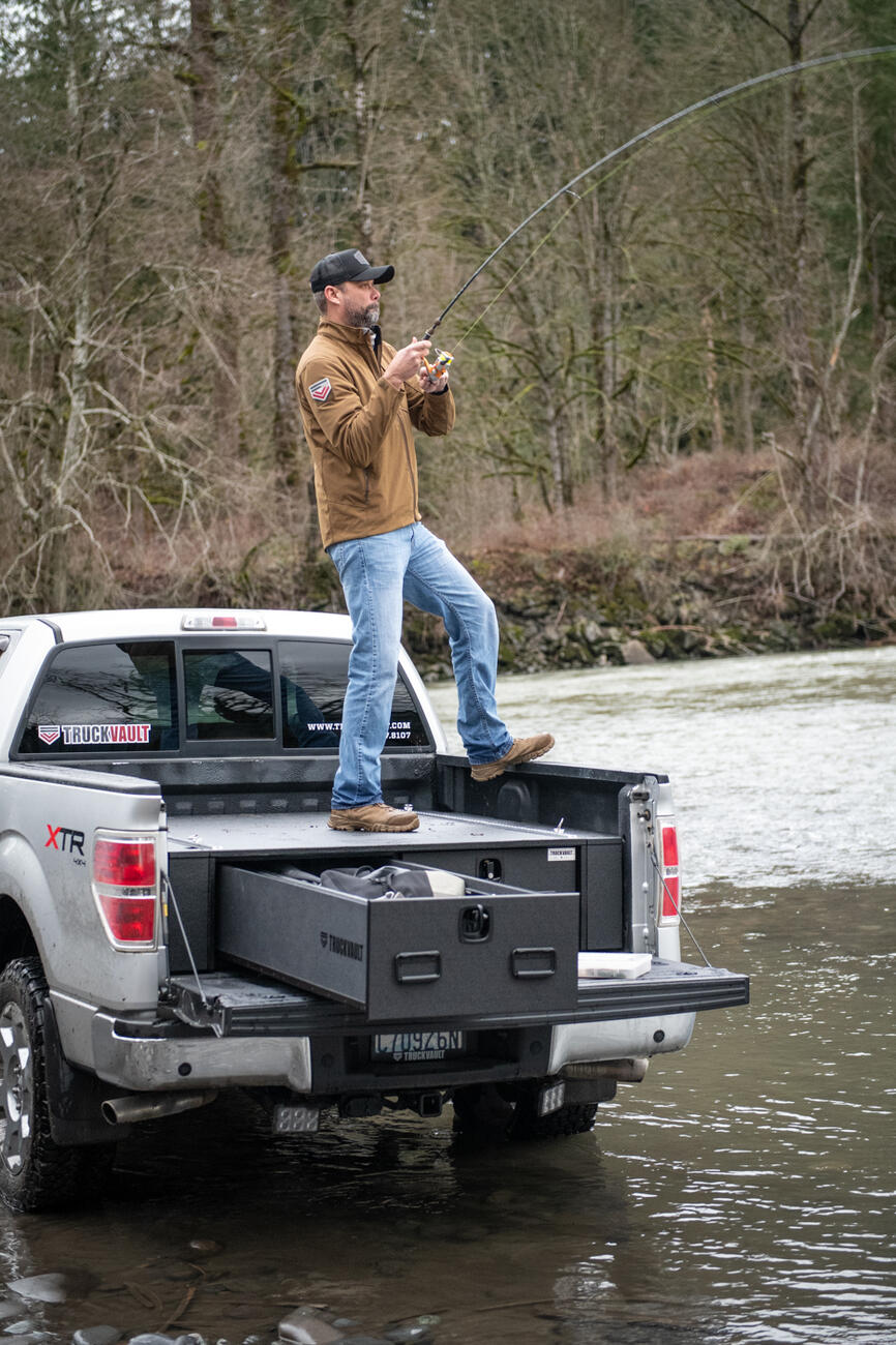 fly fishing fisherman standing on top of magnum TruckVault secure truck bed drawer system in pickup truck Ford F-150 one drawer open