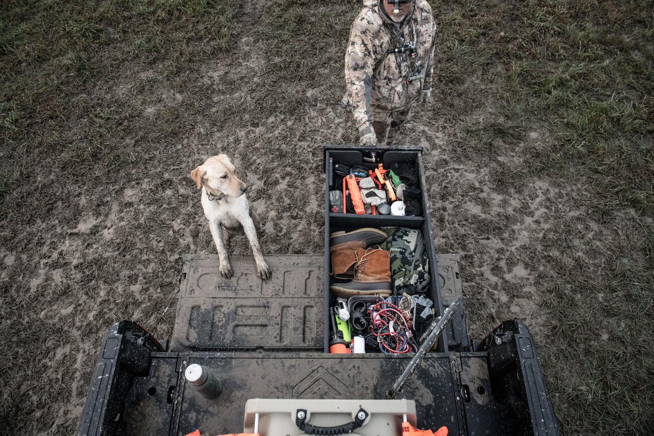 hunter opening TruckVault secure truck bed storage system in back of Ford F-150 with hunting dog nearby