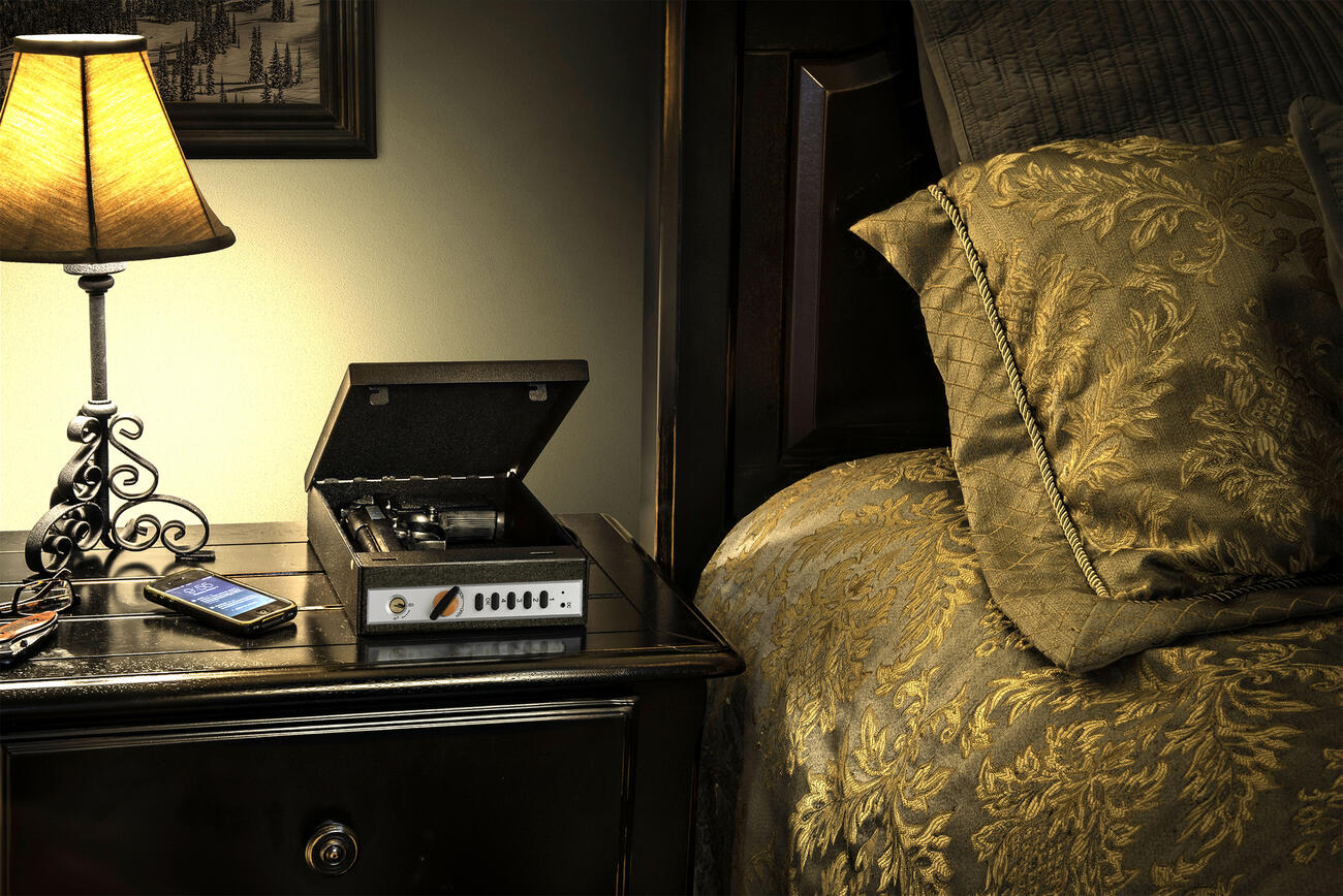 Shotlock with hand gun open on top of night stand with lit lamp