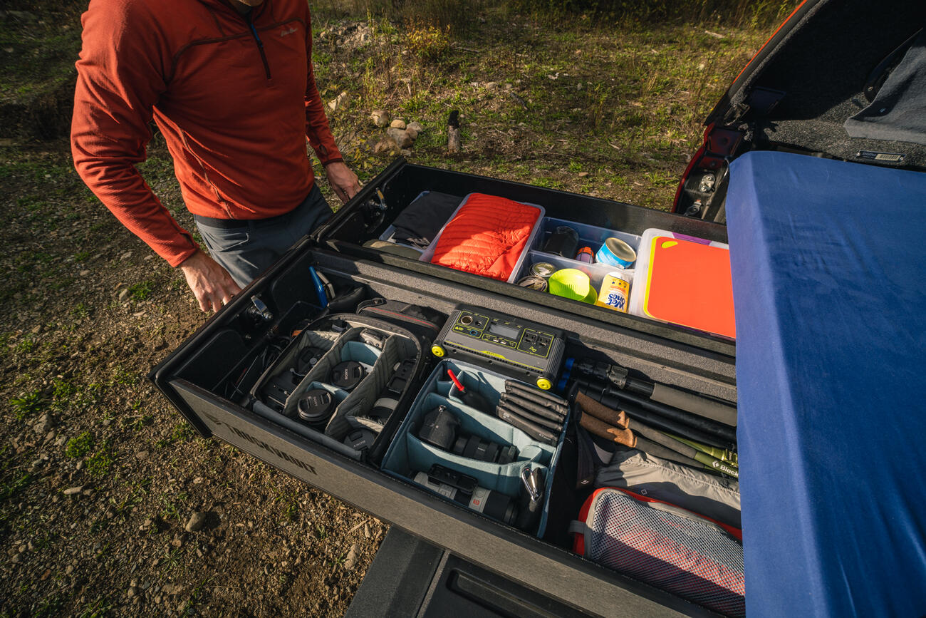 hiker opens drawers of TruckVault secure truck bed storage revealing hiking and photography gear