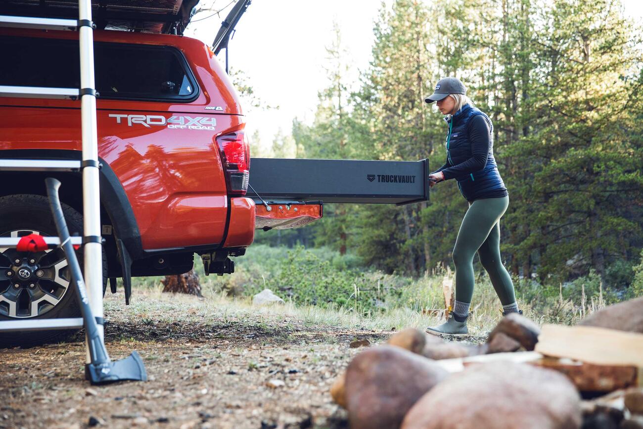 A red truck with a roof tent and a TruckVault. The TruckVault is being opened by a woman.