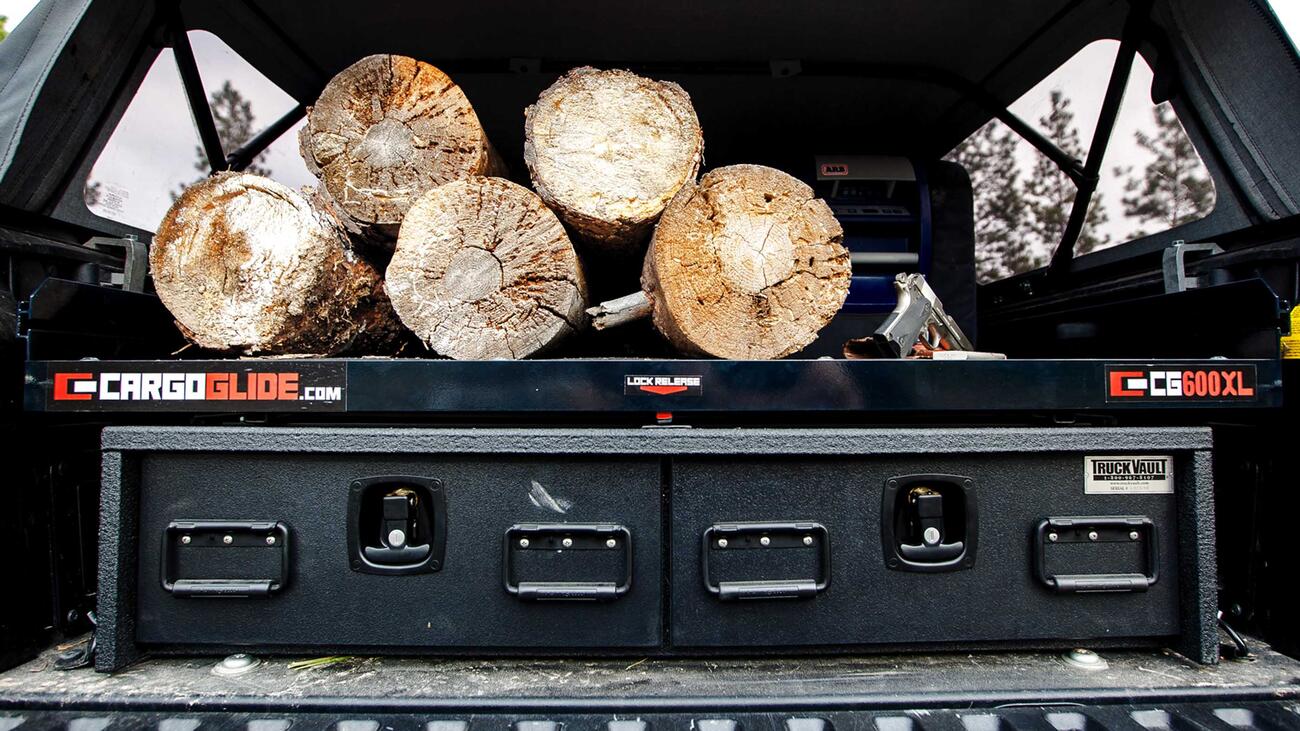 A TruckVault secure storage system in the back of a Toyota Tacoma with logs on top of the system.