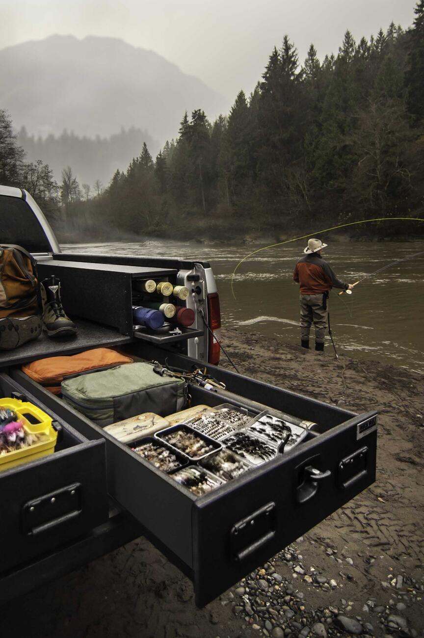A Silver Ford F-150 filled with fishing gear and a man casting a line in the background.