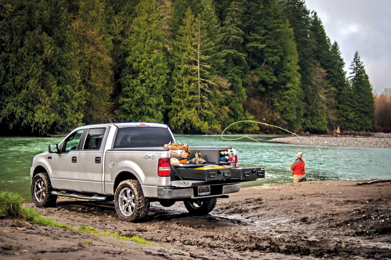 A Silver Ford F-150 filled with fishing gear and a man casting a line in the background.