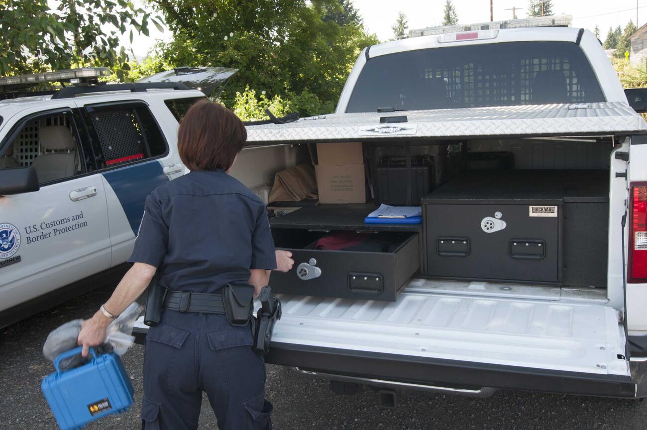 A U.S. Customs and Border Protection officer taking gear out of her White Ford F-150.