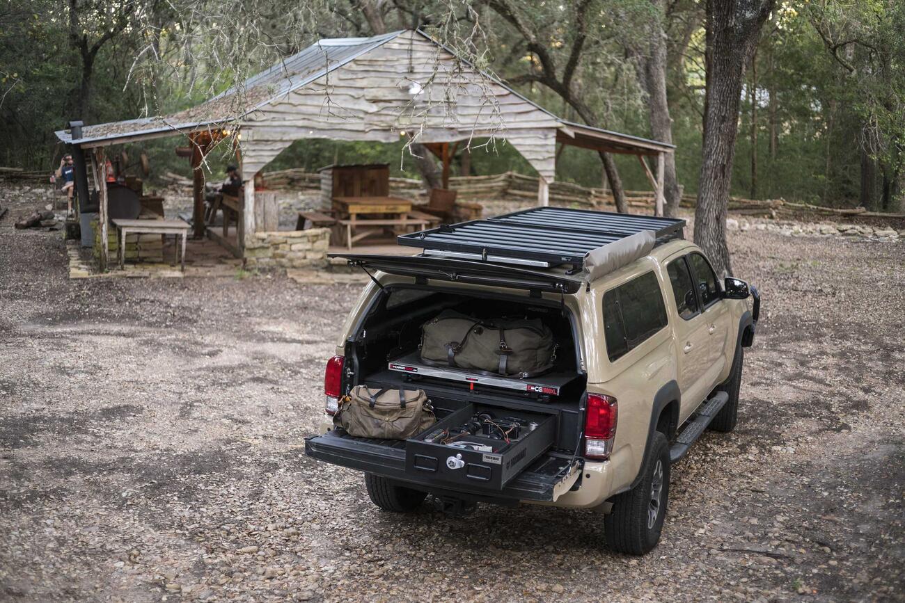 PickupSeries_CoveredBedLine_Standard2Drawer_2016_Toyota_Tacoma_TylerSharp4.jpg A Toyota Tacoma parked infront of a hut in the woods. Inside of the bed of the Tacoma is an open TruckVault filled with gear.