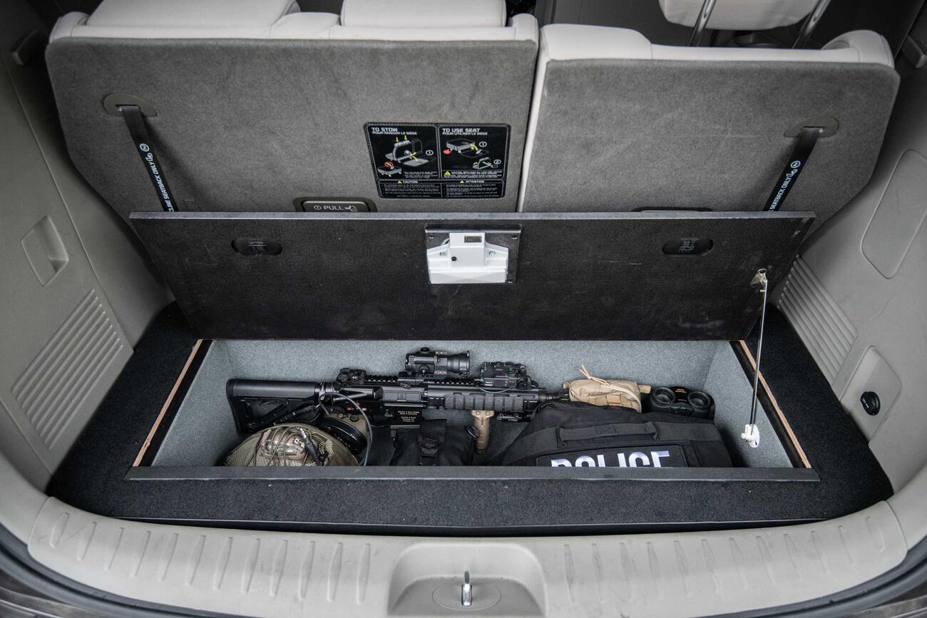 An open Kia Sedona FloorVault filled with a gun and other police gear.