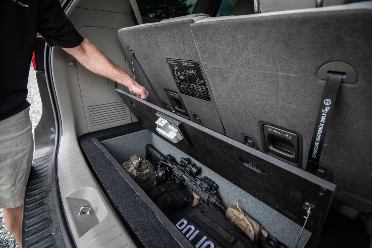 A policeman opening a Kia Sedona FloorVault with a gun and police equipment in it.