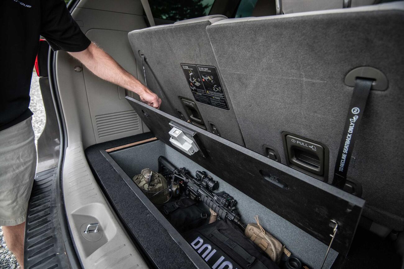 A man opening a Kia Sedona FloorVault filled with a gun and other police gear.