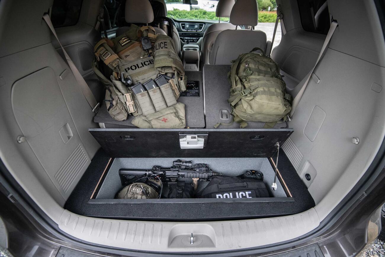 A Kia Sedona FloorVault filled with a gun and police gear. Next to two police backpacks.