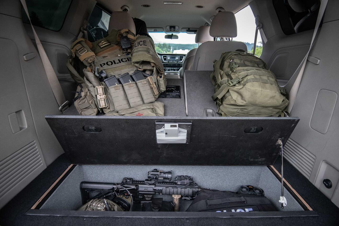 A Kia Sedona with an open SeatVualt containg a gun and police gear. Next to two police backpacks.