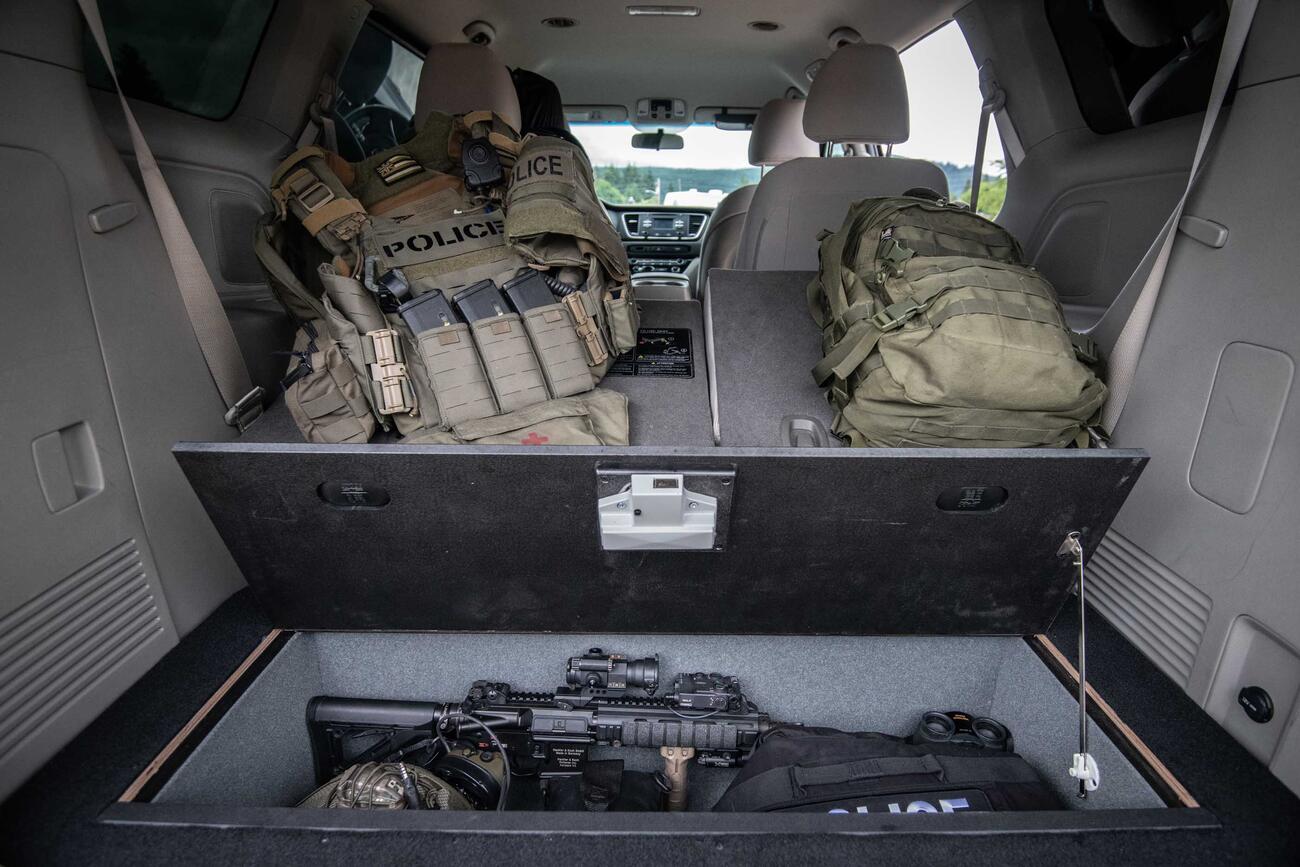 Law Enforcement A Kia Sedona with an open SeatVualt containg a gun and police gear. Next to two police backpacks.