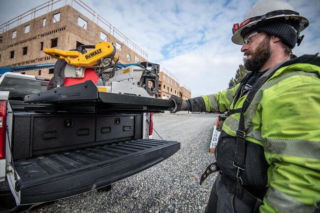 Construction worker extends a TruckGlide sliding cargo deck from a pickup truck to access large gear like a saw and ladder from his truck