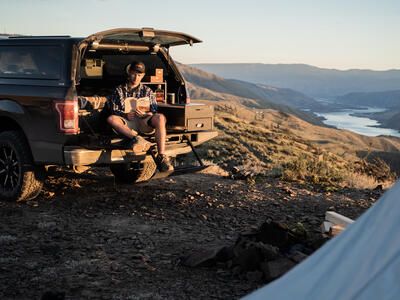 man working on laptop sitting on edge of open covered truck bed with TruckVault secure truck bed storage for camping and overlanding