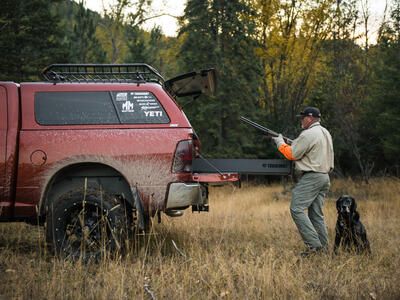 bird hunter and black dog standing in tall grass with covered Dodge Ram pickup as hunter places shotgun in TruckVault secure storage