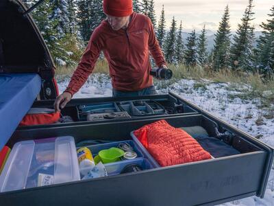snowy day as outdoorsman reaches into extended drawers of TruckVault secure storage system for SUV for camping overlanding gear