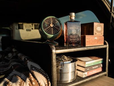books fan whiskey and camping gear sit on shelf in covered truck bed TruckVault camping overlanding storage system