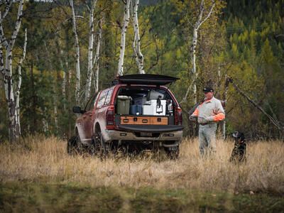 bird hunter and black dog stand in tall grass with covered Dodge Ram pickup and TruckVault secure storage
