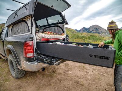 covered pickup truck with TruckVault secure storage drawer extended as outdoorsman pulls camping overlanding gear from drawer