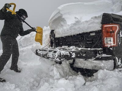 truck buried in snow as man shovels it out revealing an All Weather TruckVault secure truck bed storage system