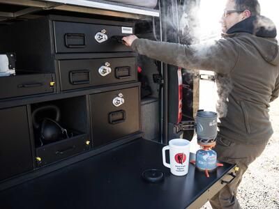 A man opening a TruckVault secure storage system while he brews coffee on a TruckVault extension table.