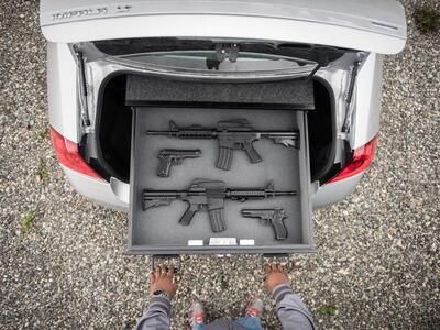 A silver Chevy Impala with a person pulling out a TruckVault drawer with guns.