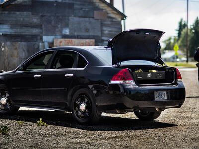 A police officer with a shotgun walking to his Impala with a TruckVault in the trunk space.