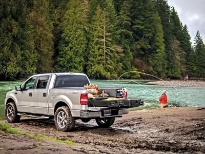 A Silver Ford F-150 filled with fishing gear and a man casting a line in the background.