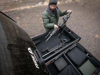 A man placing his rifle into his TruckVault which is in the back of his Ford F-150.