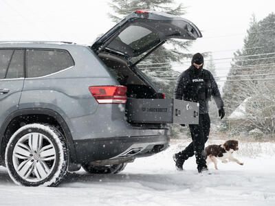 A police officer and a dog standing next to a Volkswagen Atlas with an open TruckVault in the snow.