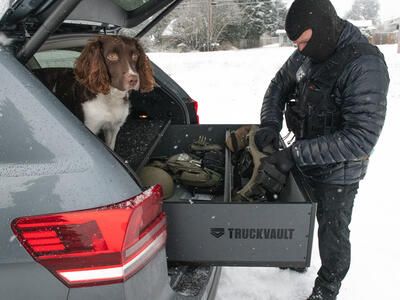 A police officer grabbing gear out of a TruckVault, with a dog sitting on top of the TruckVault.
